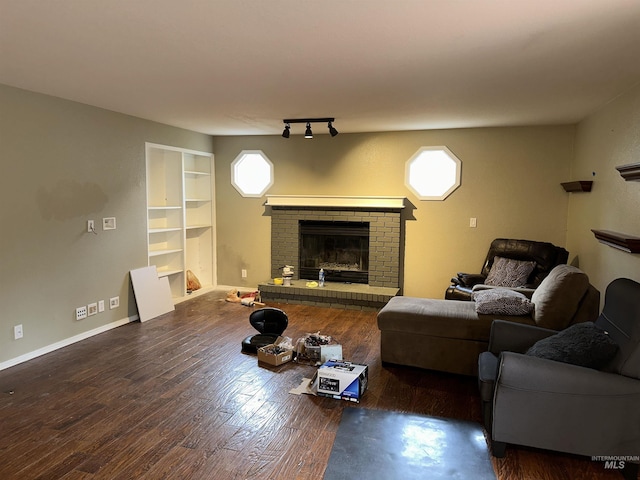 living room featuring rail lighting, dark wood-type flooring, and a brick fireplace