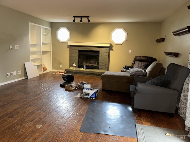 living room with rail lighting, dark wood-type flooring, and a brick fireplace