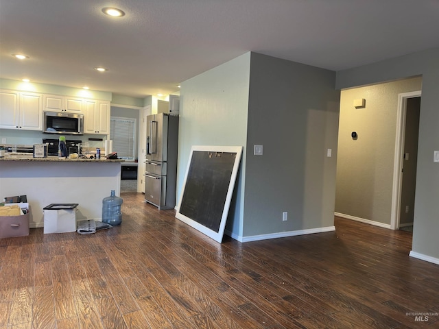 kitchen featuring dark wood-type flooring, dark stone counters, white cabinetry, kitchen peninsula, and stainless steel appliances