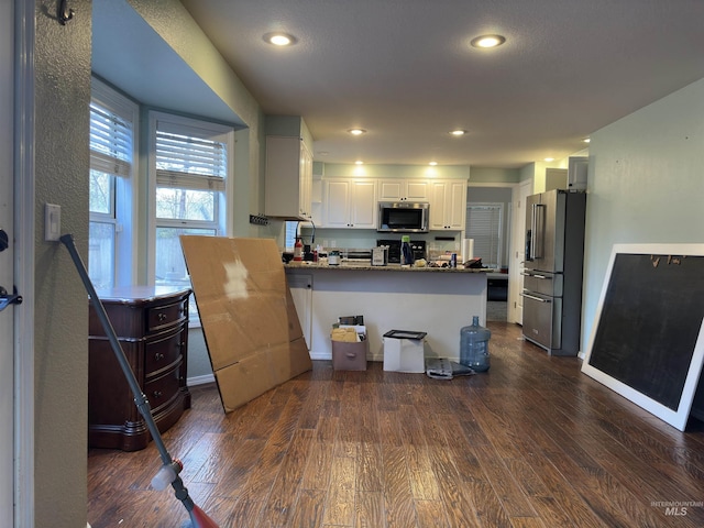 kitchen with dark wood-type flooring, stainless steel appliances, kitchen peninsula, dark stone countertops, and white cabinets