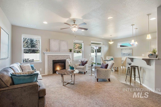 living room with light colored carpet, a fireplace, baseboards, a ceiling fan, and a textured ceiling