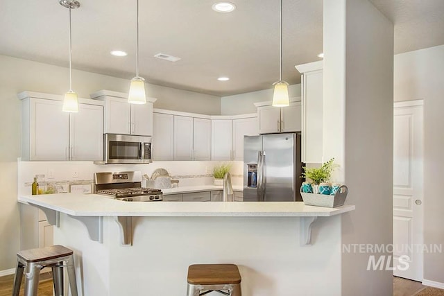 kitchen with stainless steel appliances, a kitchen bar, a peninsula, light countertops, and pendant lighting