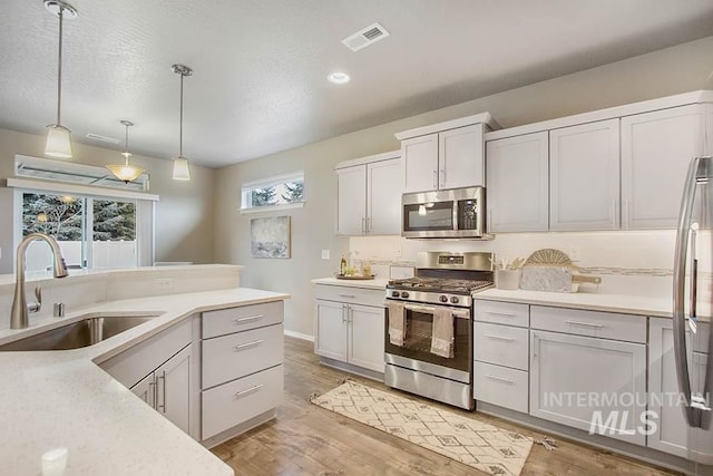 kitchen featuring appliances with stainless steel finishes, a sink, light countertops, hanging light fixtures, and recessed lighting