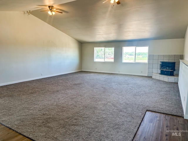 unfurnished living room featuring lofted ceiling, carpet, ceiling fan, and a wood stove