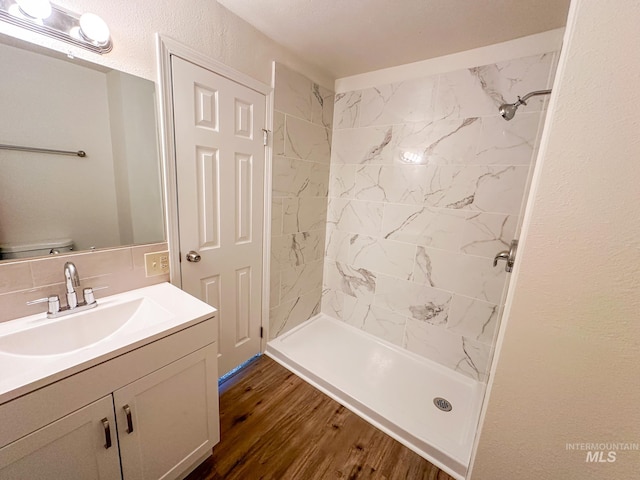 bathroom with hardwood / wood-style flooring, vanity, toilet, and a tile shower