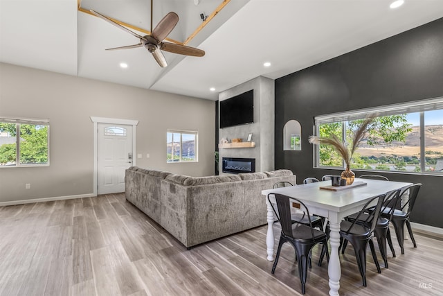 living room featuring ceiling fan, a large fireplace, light wood-type flooring, and plenty of natural light