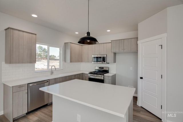 kitchen with sink, a center island, light hardwood / wood-style flooring, pendant lighting, and appliances with stainless steel finishes