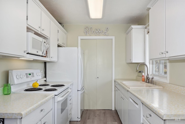 kitchen with white appliances, light countertops, white cabinetry, a sink, and light wood-style flooring