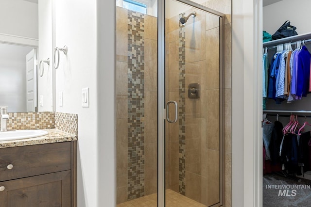 bathroom featuring backsplash, an enclosed shower, and vanity