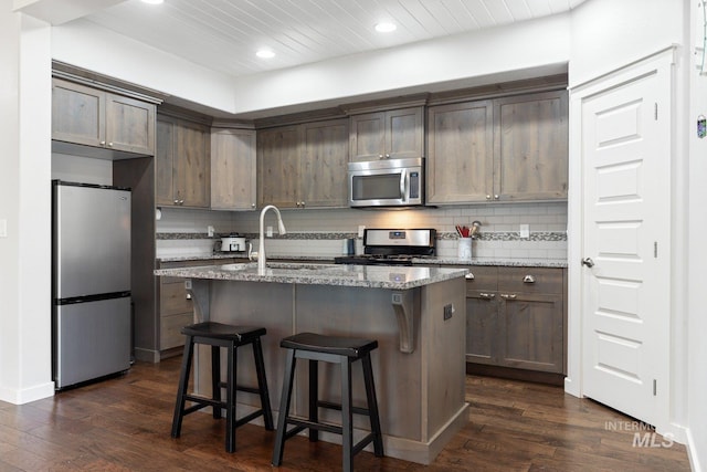 kitchen with light stone countertops, sink, stainless steel appliances, a center island with sink, and dark hardwood / wood-style floors