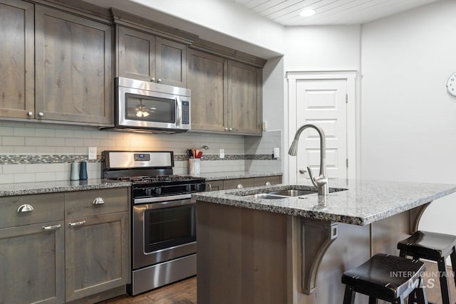 kitchen with tasteful backsplash, light stone counters, a kitchen island with sink, a breakfast bar, and stainless steel appliances