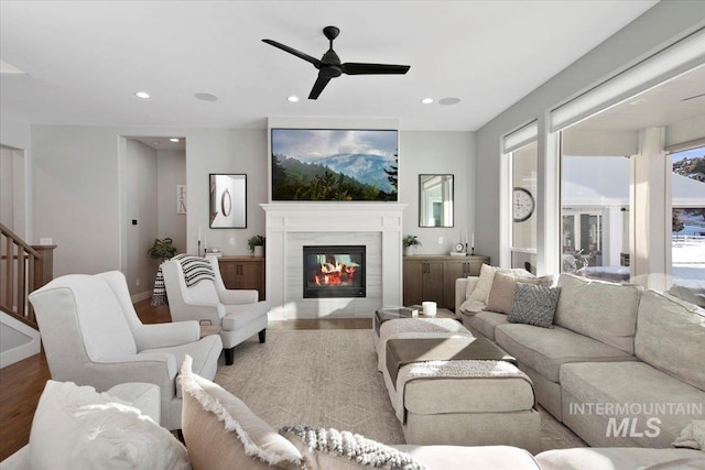 living area featuring a ceiling fan, a glass covered fireplace, light wood-style flooring, stairway, and recessed lighting