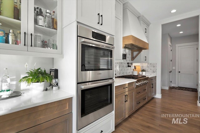 kitchen with stainless steel appliances, white cabinetry, light countertops, glass insert cabinets, and custom range hood