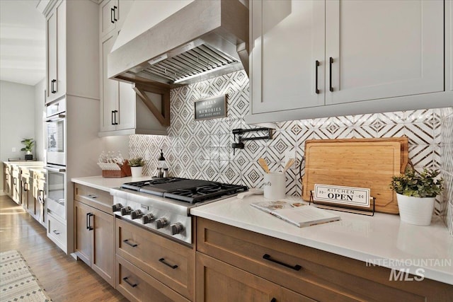 kitchen featuring light countertops, appliances with stainless steel finishes, white cabinetry, and custom range hood