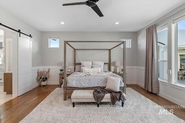 bedroom with a wainscoted wall, recessed lighting, a barn door, ceiling fan, and wood finished floors