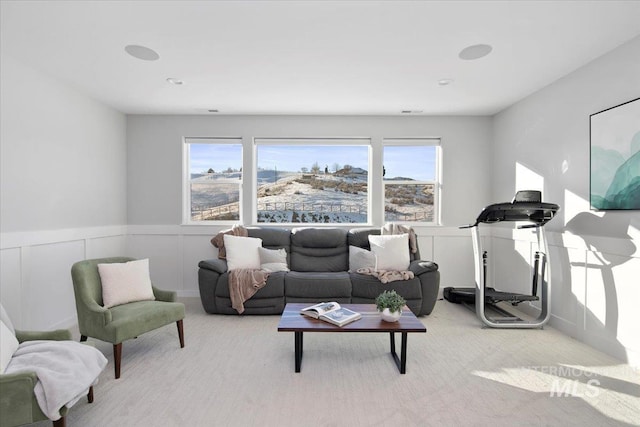 living room featuring light carpet, wainscoting, and a decorative wall