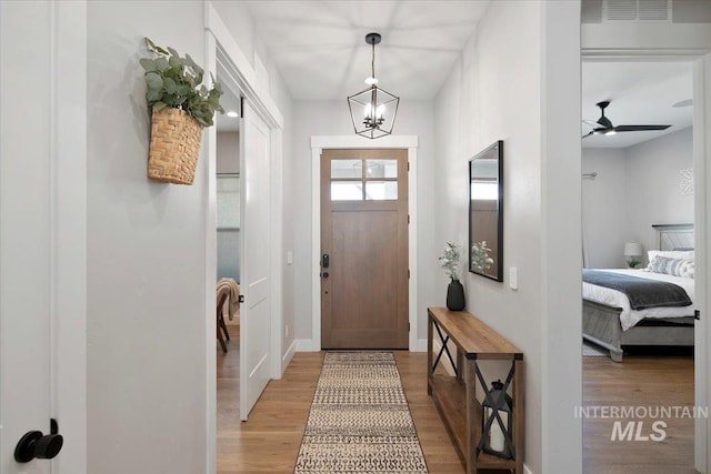 entryway with ceiling fan with notable chandelier, wood finished floors, visible vents, and baseboards