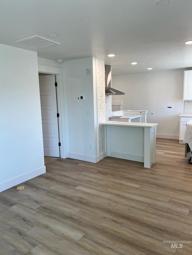 kitchen with light hardwood / wood-style floors, wall chimney range hood, a breakfast bar area, and kitchen peninsula