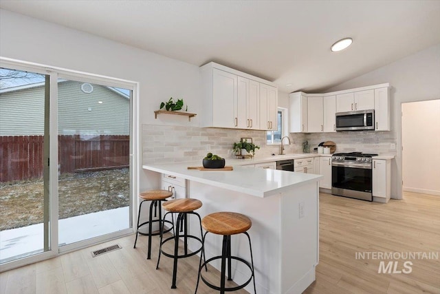 kitchen with stainless steel appliances, light countertops, visible vents, white cabinets, and a kitchen breakfast bar