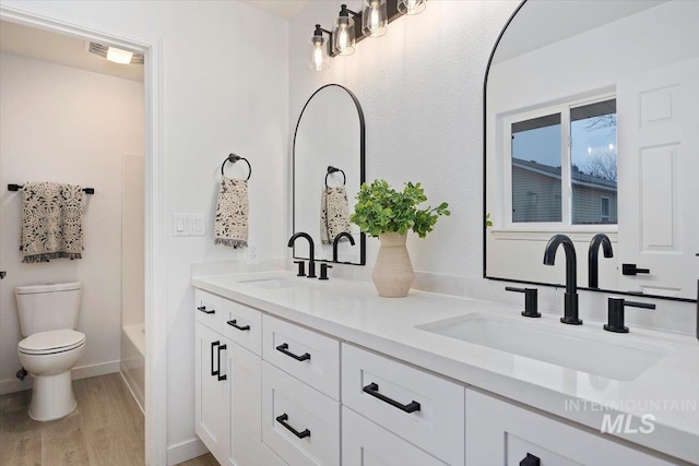 full bath featuring double vanity, wood finished floors, a sink, and toilet