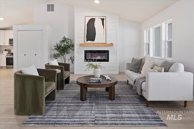 living room featuring a large fireplace, visible vents, lofted ceiling, wood finished floors, and recessed lighting