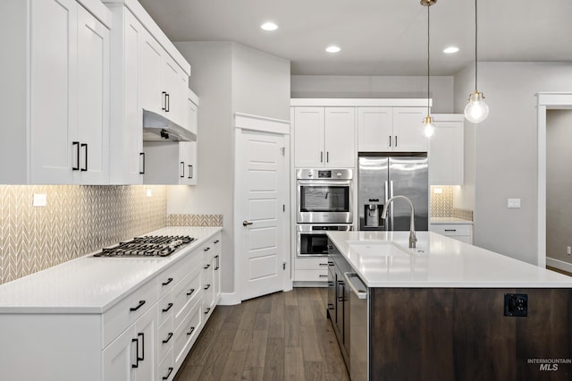 kitchen featuring backsplash, white cabinets, a center island with sink, sink, and appliances with stainless steel finishes