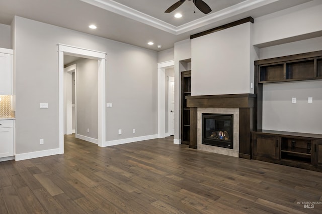 unfurnished living room featuring ceiling fan, ornamental molding, dark wood-type flooring, and a tile fireplace