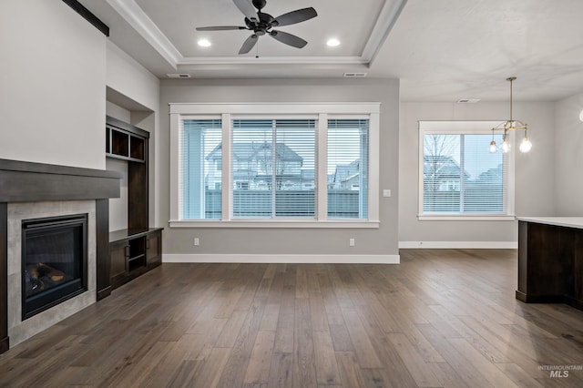 unfurnished living room with a raised ceiling, a tile fireplace, dark wood-type flooring, and ceiling fan with notable chandelier