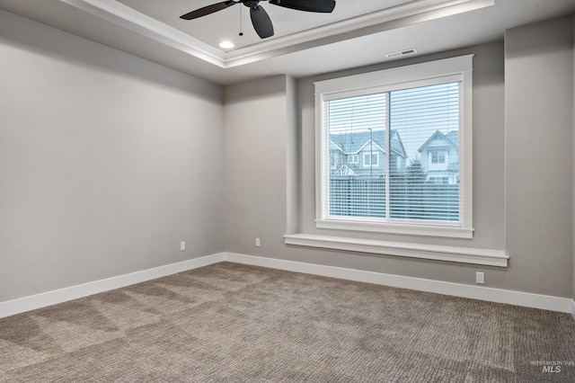 empty room with a tray ceiling, ceiling fan, and carpet flooring