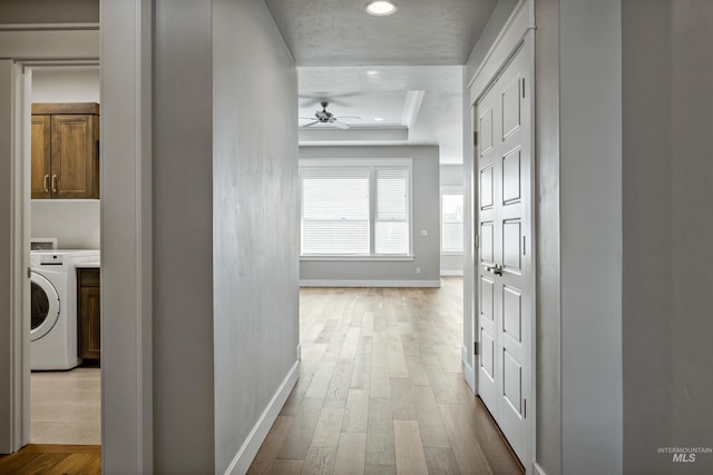 hall featuring washer / clothes dryer, a tray ceiling, and light hardwood / wood-style floors