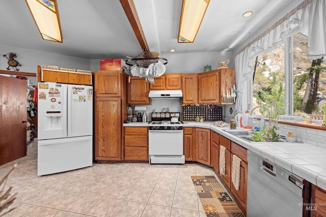 kitchen with sink, tile countertops, light tile patterned floors, white appliances, and backsplash