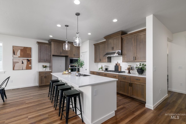 kitchen featuring appliances with stainless steel finishes, dark hardwood / wood-style flooring, tasteful backsplash, a center island with sink, and hanging light fixtures