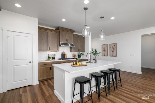 kitchen with gas cooktop, an island with sink, decorative light fixtures, decorative backsplash, and a breakfast bar