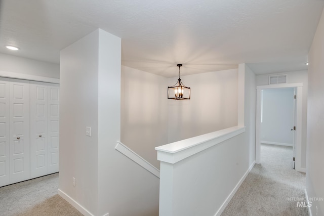 corridor featuring light carpet and an inviting chandelier