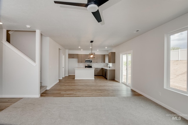 kitchen with tasteful backsplash, hanging light fixtures, ceiling fan, a kitchen island, and light hardwood / wood-style flooring