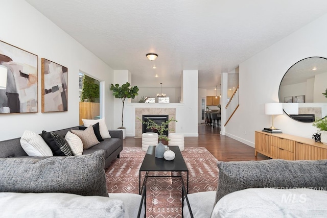 living room with a textured ceiling, a tile fireplace, dark wood-type flooring, baseboards, and stairs