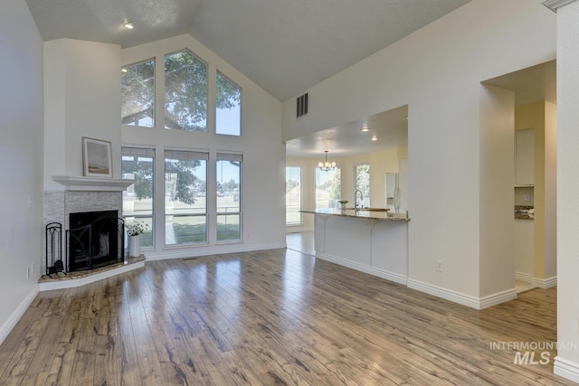 12335 W Red Spruce, Boise, ID 83713 - unfurnished living room featuring wood-type flooring, high vaulted ceiling, a fireplace with raised hearth, plenty of natural light, and a chandelier