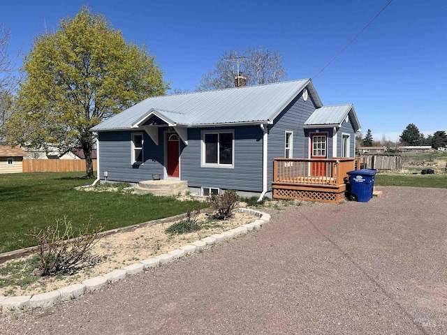 view of front facade with a front yard, metal roof, a chimney, fence, and a wooden deck