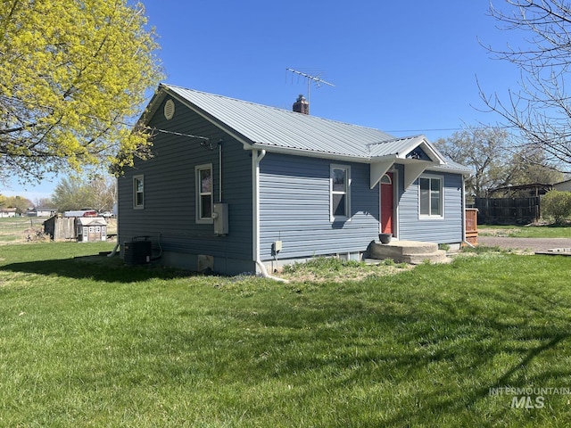 view of front of property with a front yard, metal roof, a chimney, fence, and cooling unit