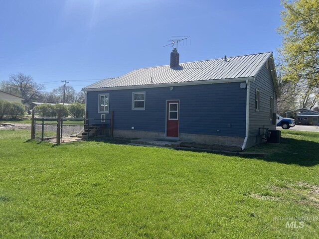 rear view of house featuring a chimney, metal roof, central AC unit, and a lawn