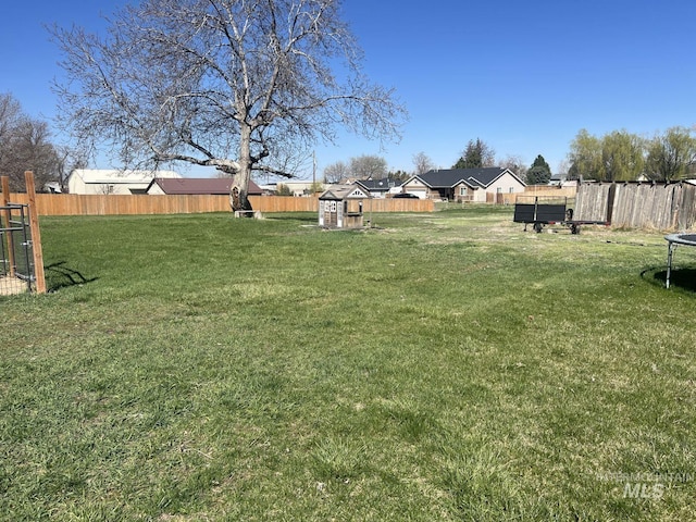 view of yard with a storage shed, a trampoline, a fenced backyard, and an outbuilding