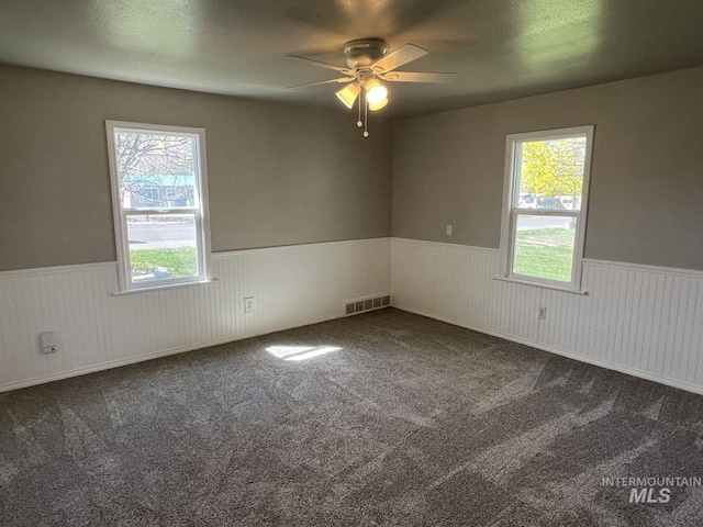 unfurnished room featuring visible vents, ceiling fan, wainscoting, and a healthy amount of sunlight