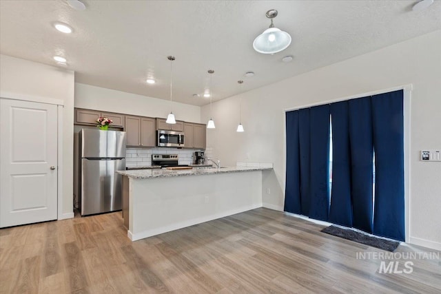 2312 E Spice Loop Unit 3, Nampa, ID 83687 - kitchen featuring appliances with stainless steel finishes, decorative backsplash, light wood-style flooring, a peninsula, and hanging light fixtures
