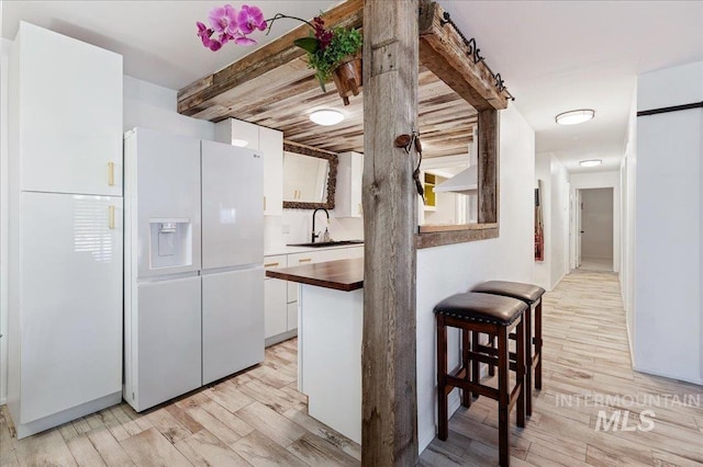 kitchen featuring sink, white cabinets, white fridge with ice dispenser, a barn door, and light wood-type flooring