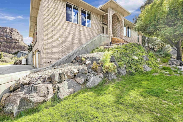 view of property exterior featuring brick siding, a lawn, and driveway