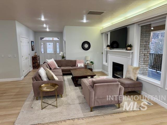 living room with visible vents, light wood-style flooring, a fireplace, and baseboards