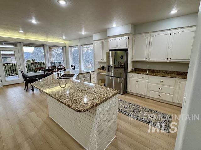 kitchen featuring dark stone countertops, light wood-style flooring, stainless steel fridge with ice dispenser, a sink, and white cabinets