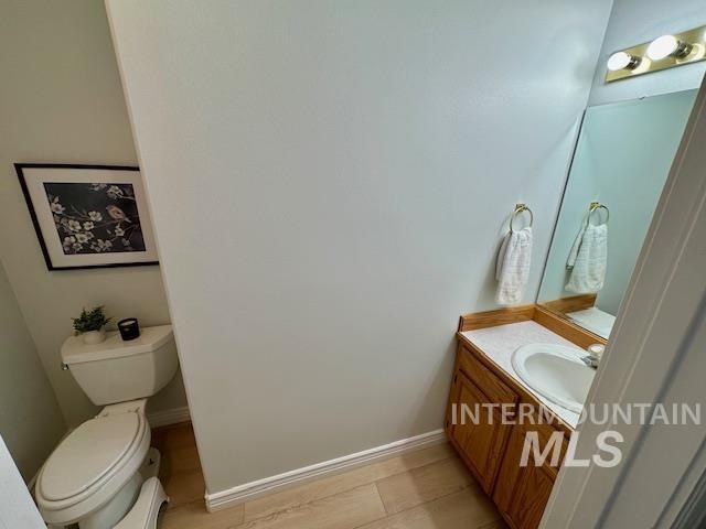 half bathroom with baseboards, toilet, and vanity