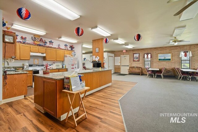 kitchen featuring brick wall, kitchen peninsula, white appliances, ceiling fan, and light carpet