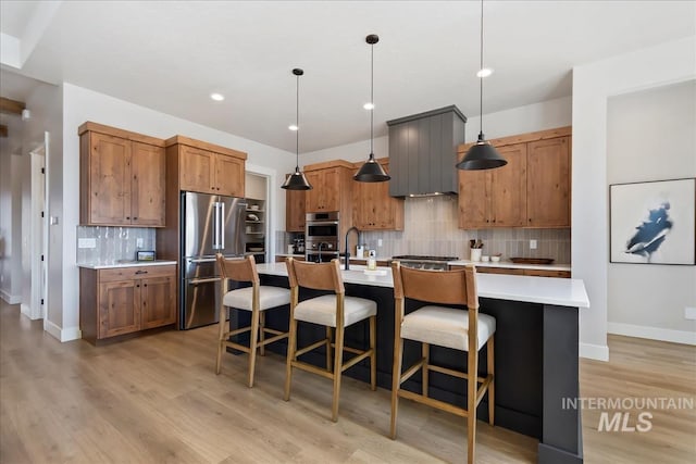 kitchen featuring appliances with stainless steel finishes, backsplash, light countertops, light wood-style floors, and hanging light fixtures